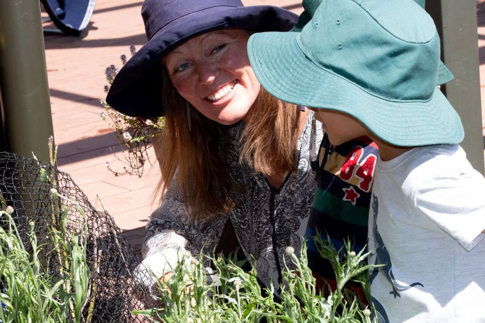 Two people examining plants and flowers in a garden while wearing sun hats.