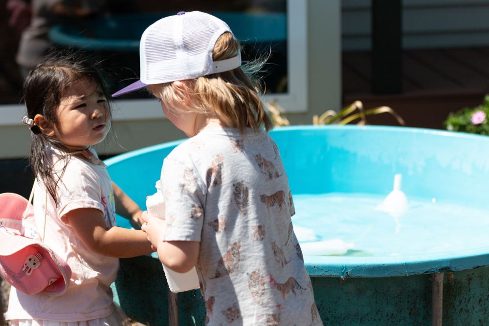 Children playing with water toys near a blue inflatable pool on a sunny day.