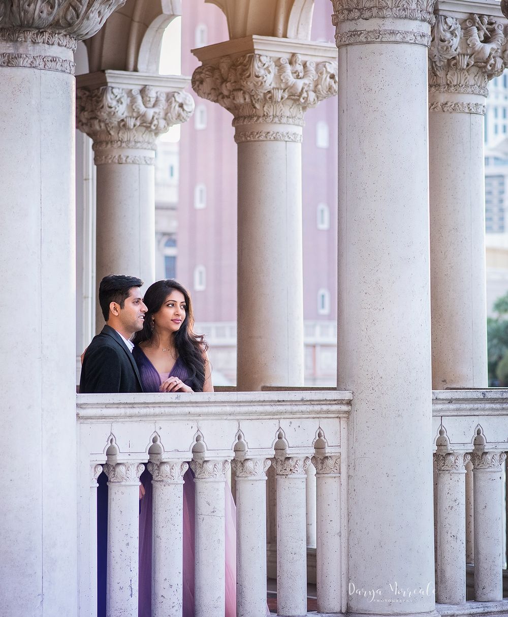 A couple stands between classical white columns in an elegant architectural setting.
