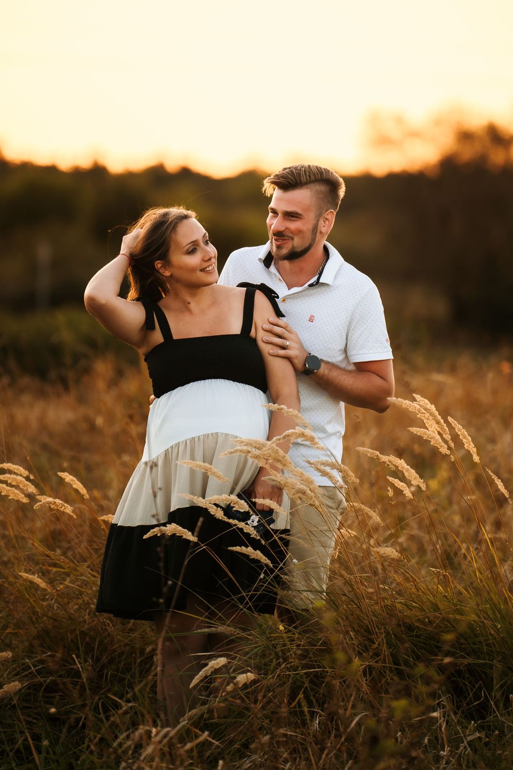Intimate moment between couple standing in tall grass during golden hour photo session.