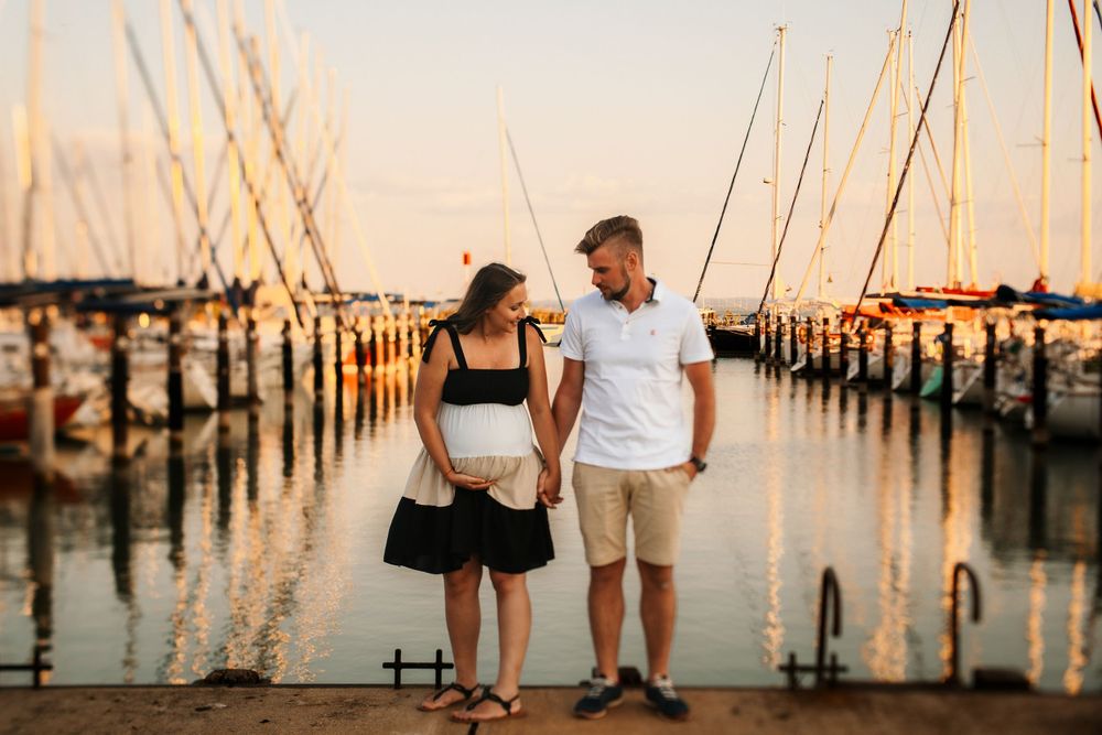 Couple standing on marina dock at sunset with boats and masts in background.