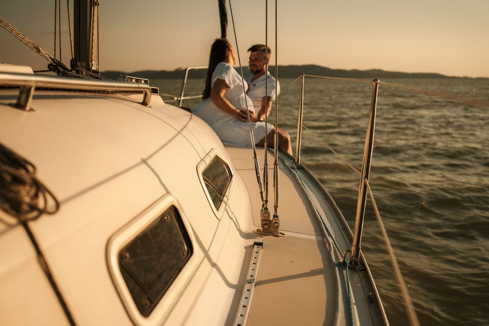 A romantic couple sits together on a sailboat deck during golden hour on calm waters.