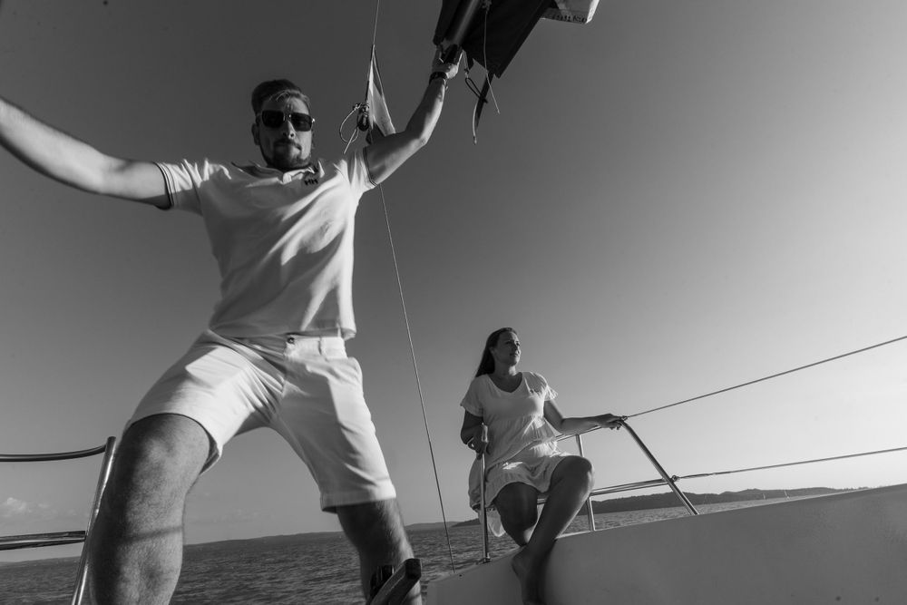 Black and white shot of sailors adjusting ropes on a boat deck against the sea.