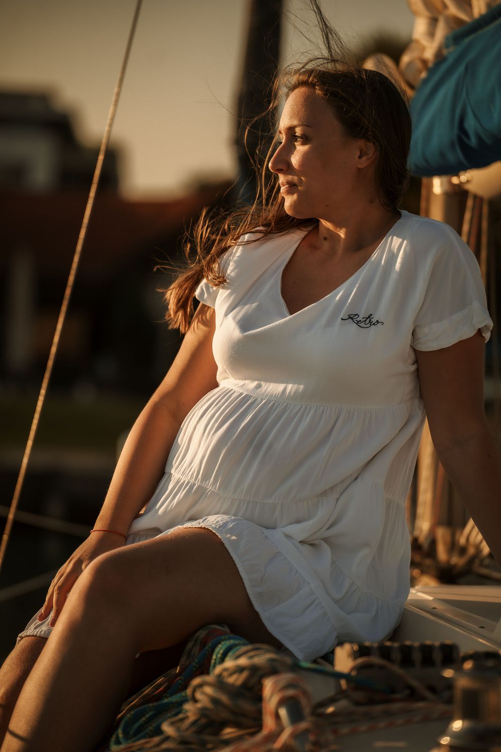 Person in white dress sitting on sailboat deck during golden hour sunset.