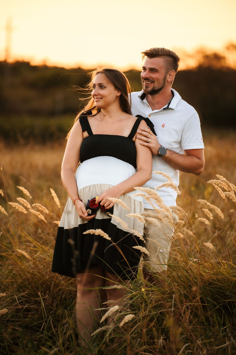 Romantic sunset photoshoot of a couple in a field of tall grass with golden light behind them.