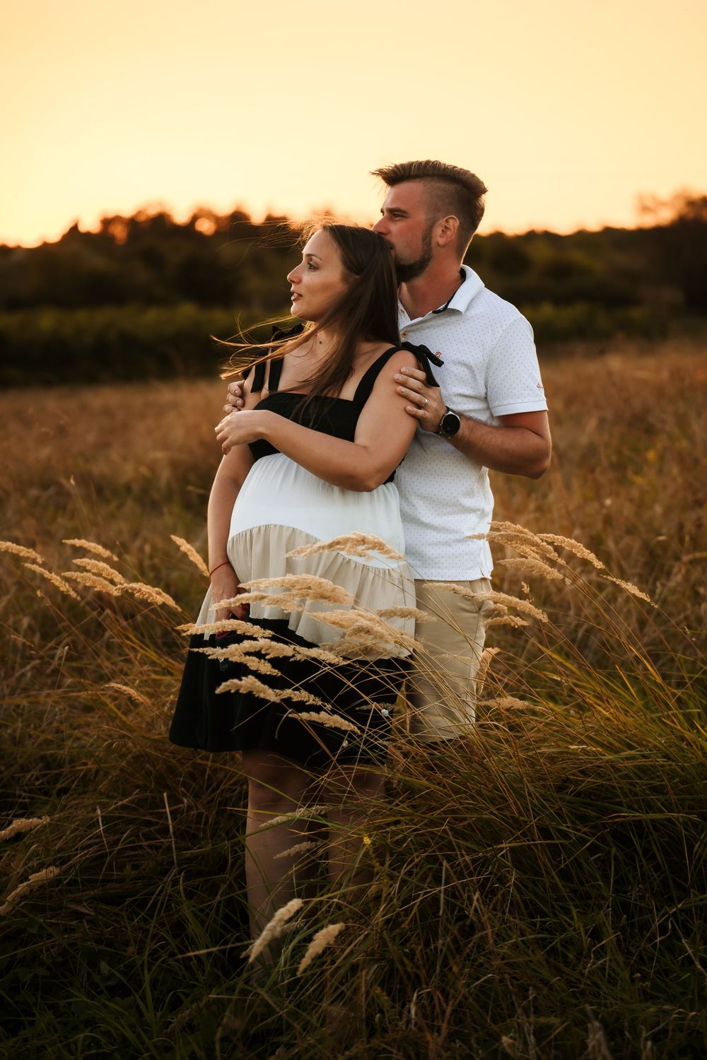 An intimate maternity portrait in a sun-drenched field at golden hour.