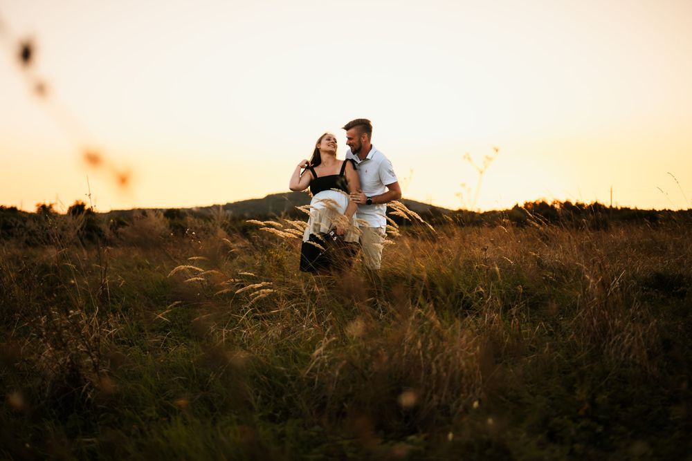 A couple dances together in a field during sunset maternity photography session.