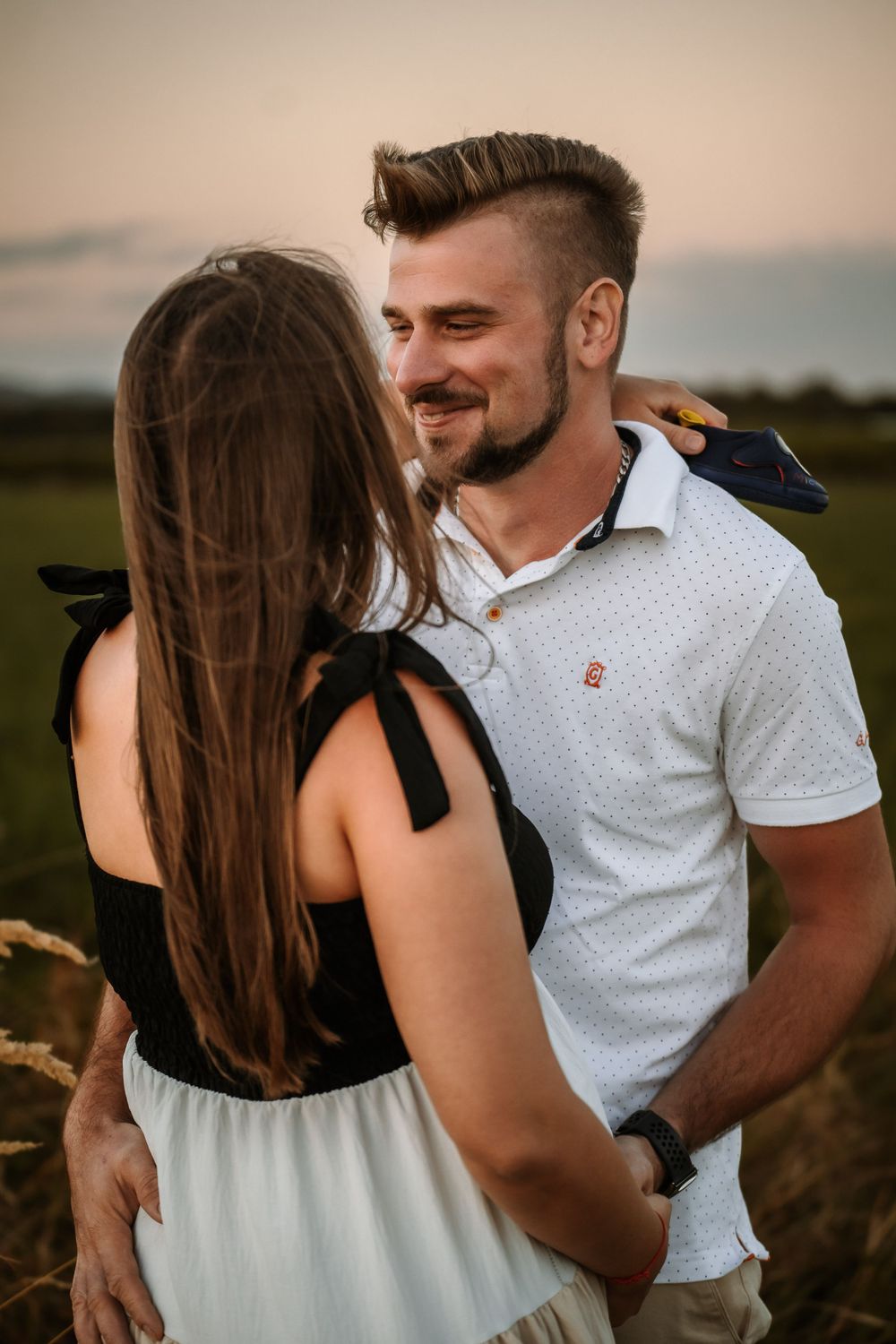 Couple embraces in outdoor field during golden hour photography session.