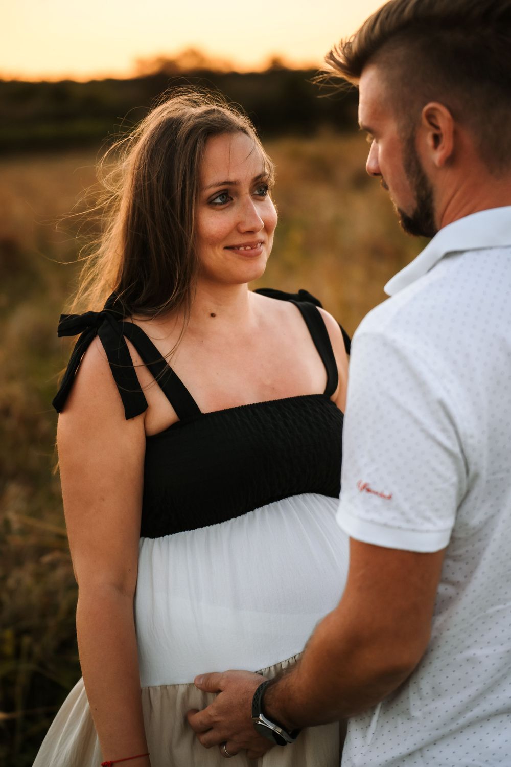 Couple shares intimate moment in field during golden hour maternity photoshoot.