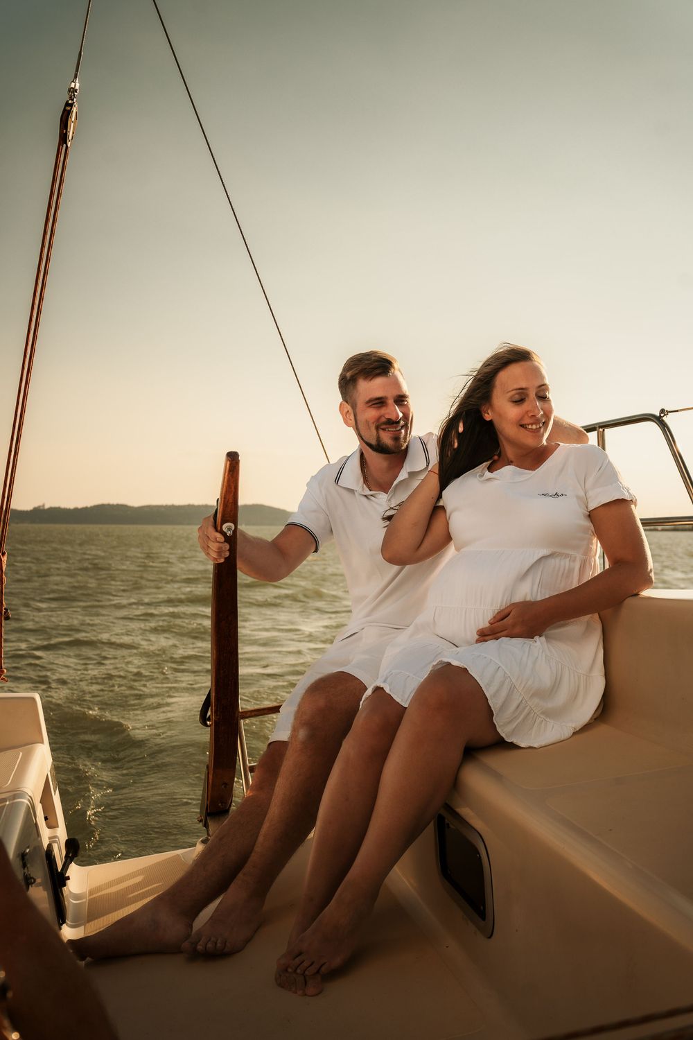 A couple in white outfits enjoying a romantic sunset sailing trip together on a yacht.