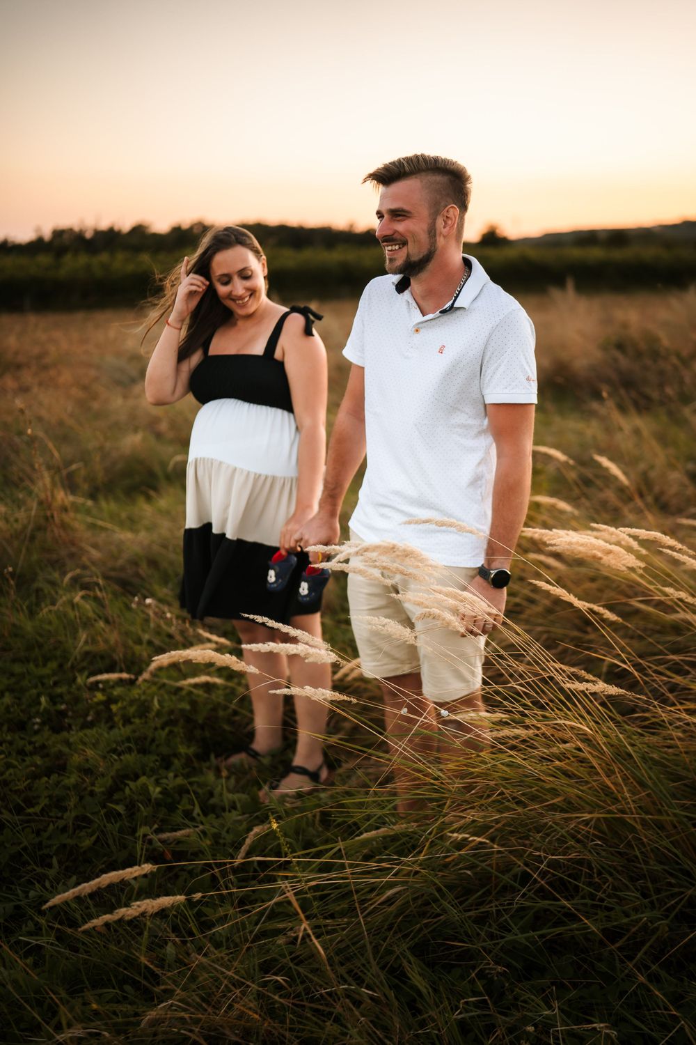 Couple walking through tall grass field during golden hour sunset photo session.