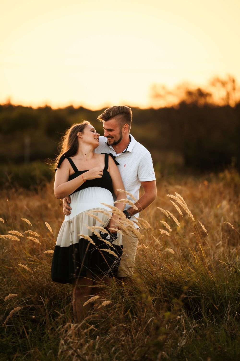 Couple embracing in field of wheat during warm sunset photoshoot.