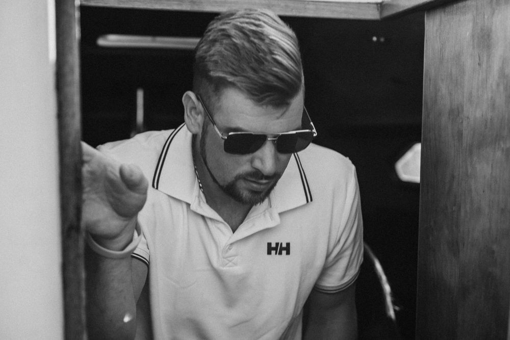 A casual black and white portrait on a boat wearing sunglasses and a white polo.