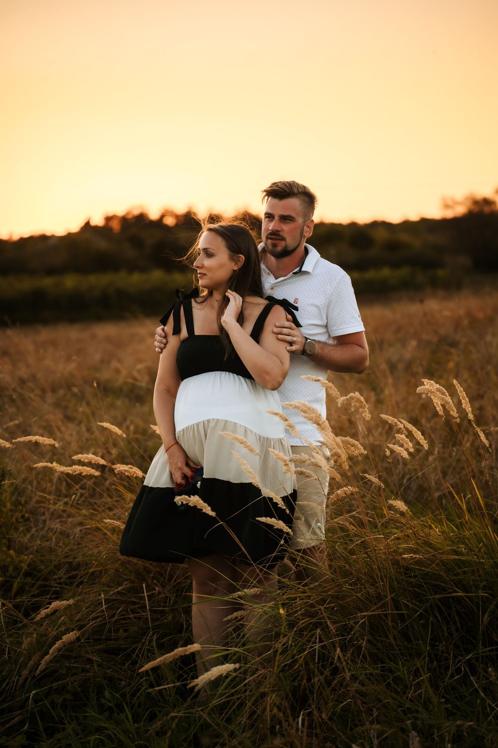 A couple poses in golden wheat field during sunset maternity session.