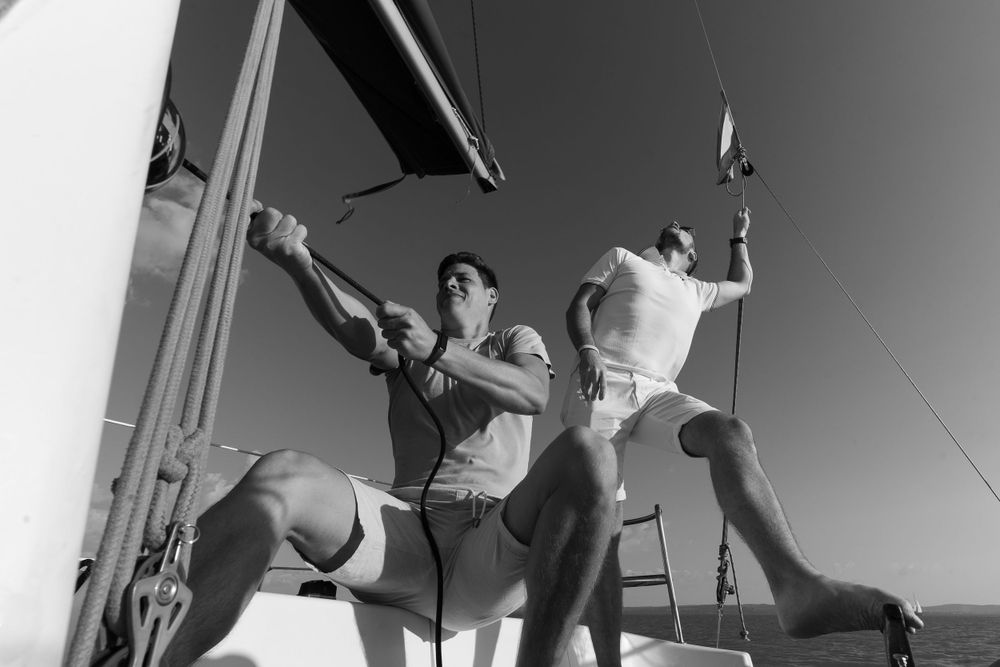 Black and white action shot of people working with ropes and rigging on a sailboat.