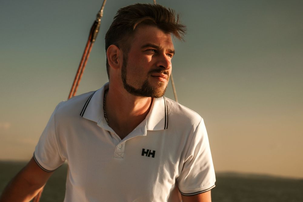 Person in a white Helly Hansen polo shirt sailing during sunset.