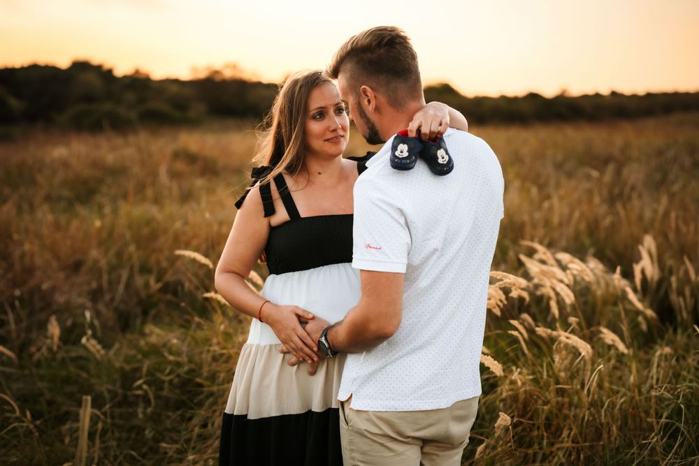 Couple poses in golden field during sunset maternity session.