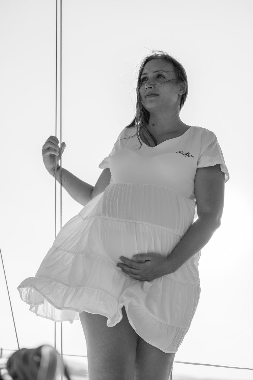 Woman in white dress holds sailing rope while standing on boat deck.