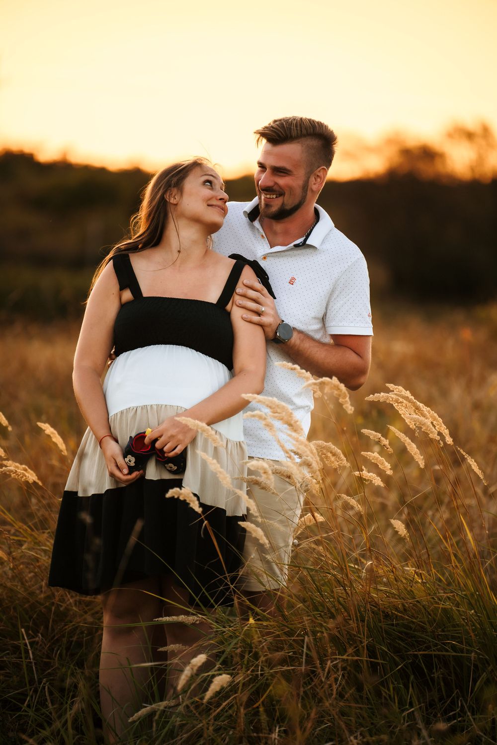 A joyful maternity moment captured in tall grass during sunset.