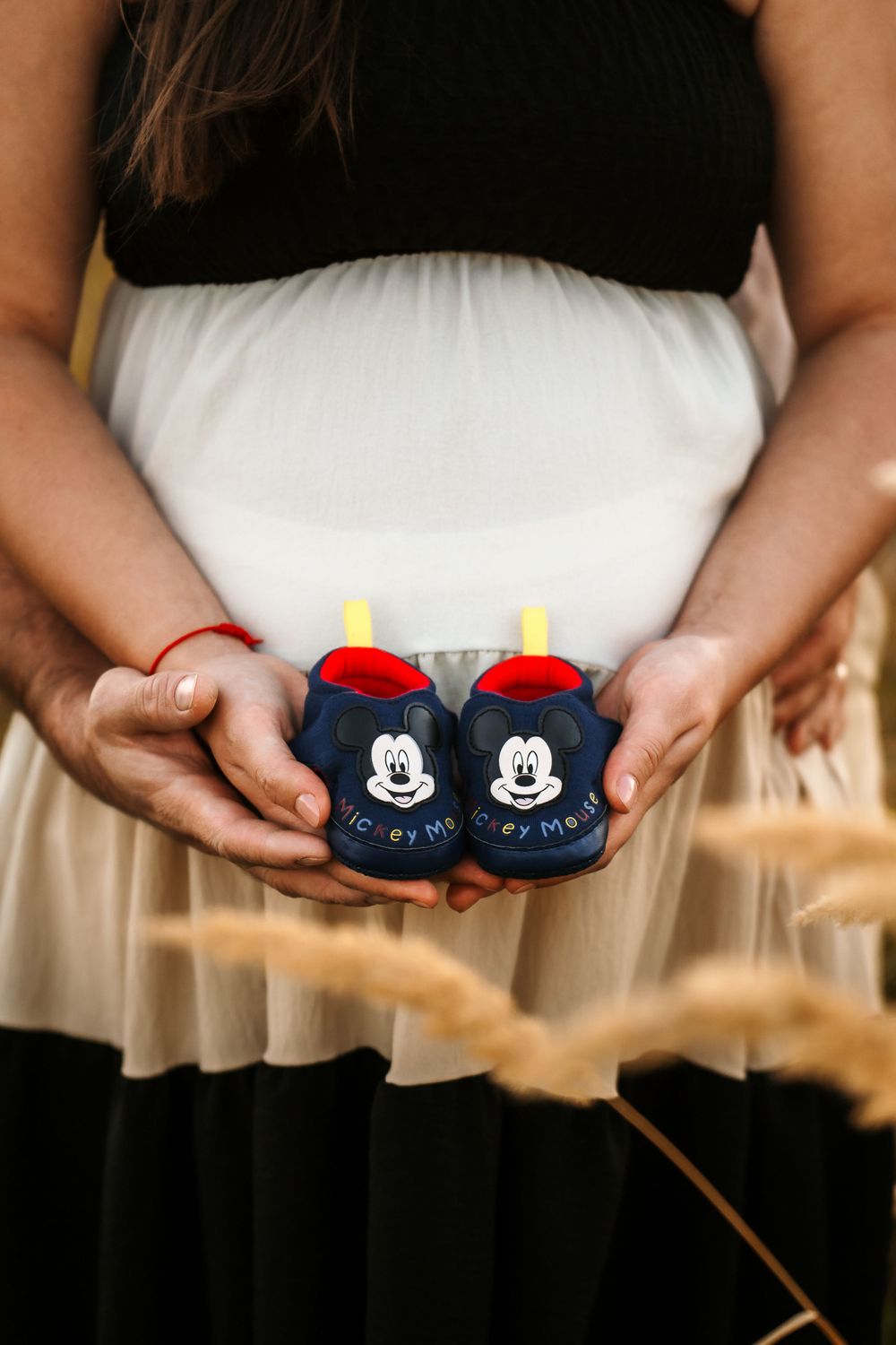 Hands holding tiny Mickey Mouse baby booties against black and white dress.