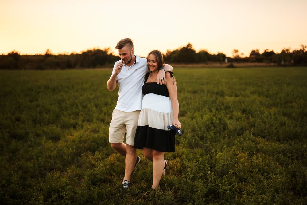 A couple strolls through a green meadow during golden hour.