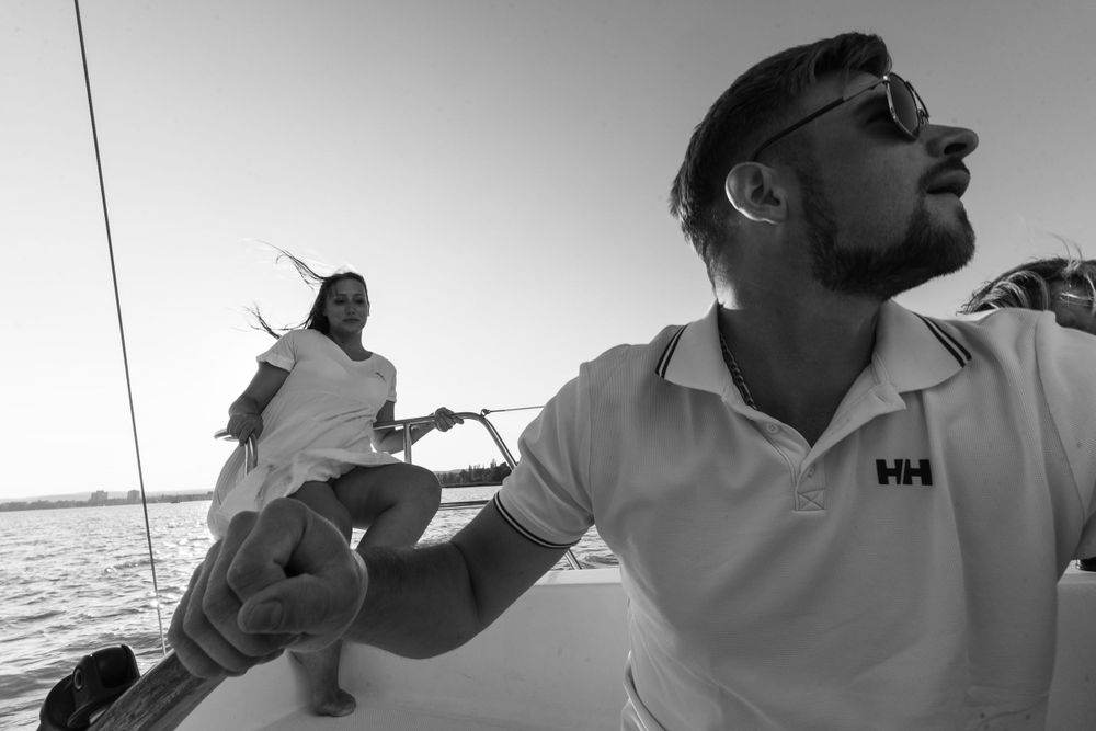 Two people sailing on a yacht in black and white as they navigate across open waters.