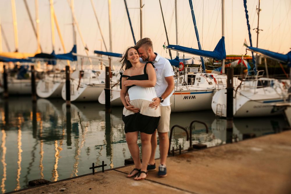 Romantic moment between couple on marina dock with boats and sunset reflections.