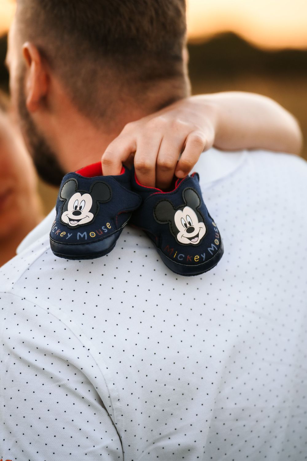 Close-up of Mickey Mouse baby shoes held against white polka dot shirt.