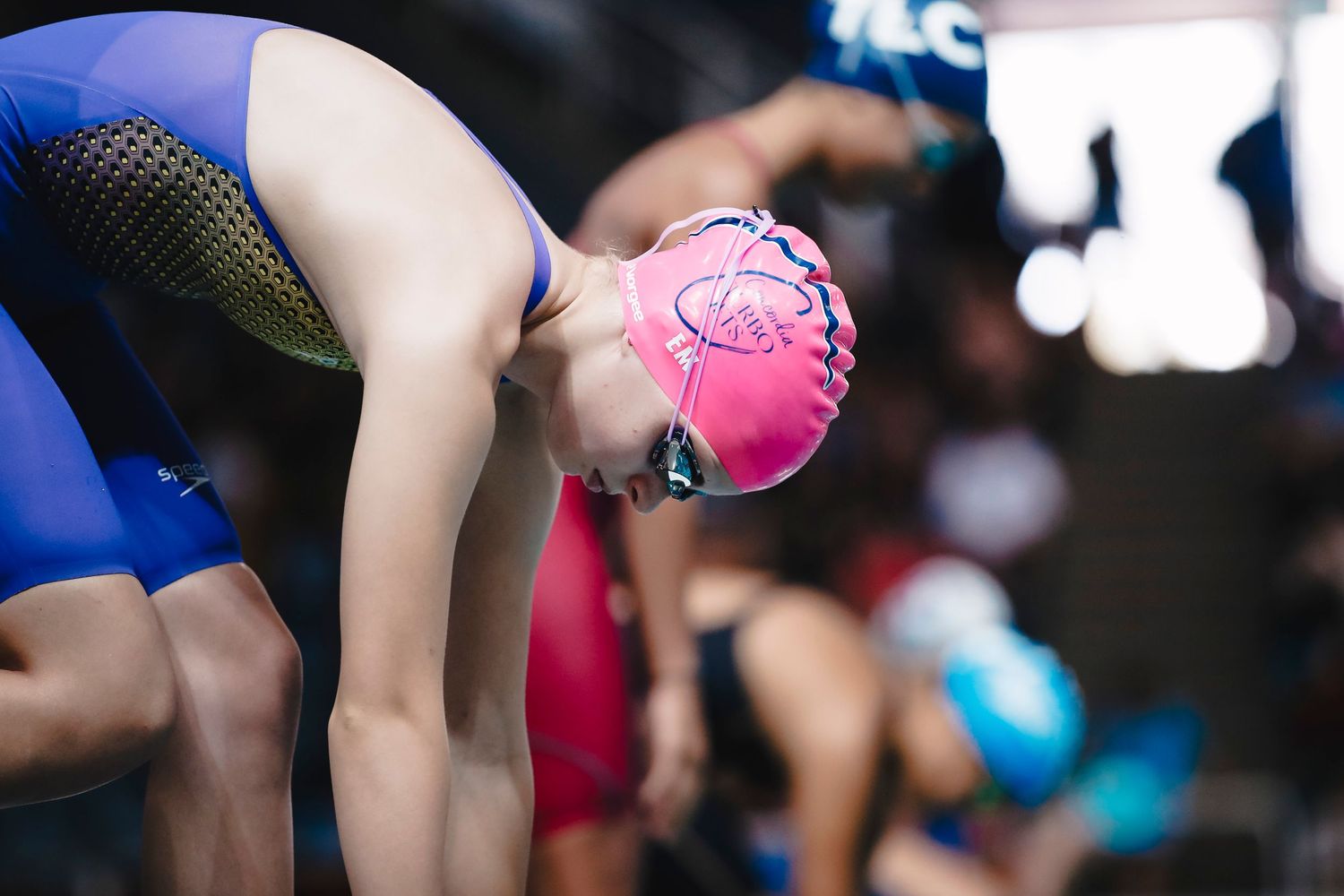 Swimmer in blue suit and pink cap preparing to dive from starting block.