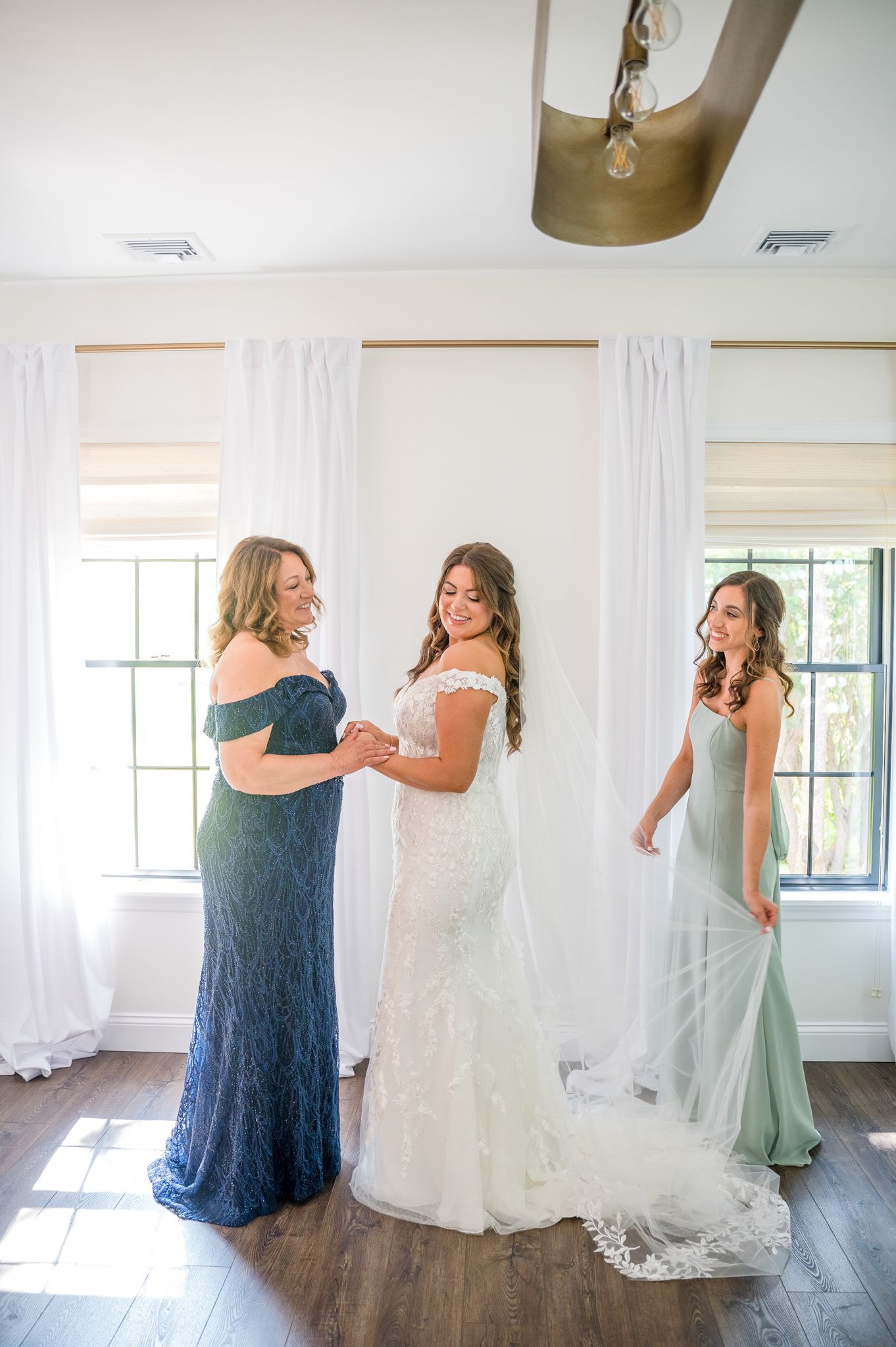 Bride holding hands with her mother as maid of honor fixes veil.