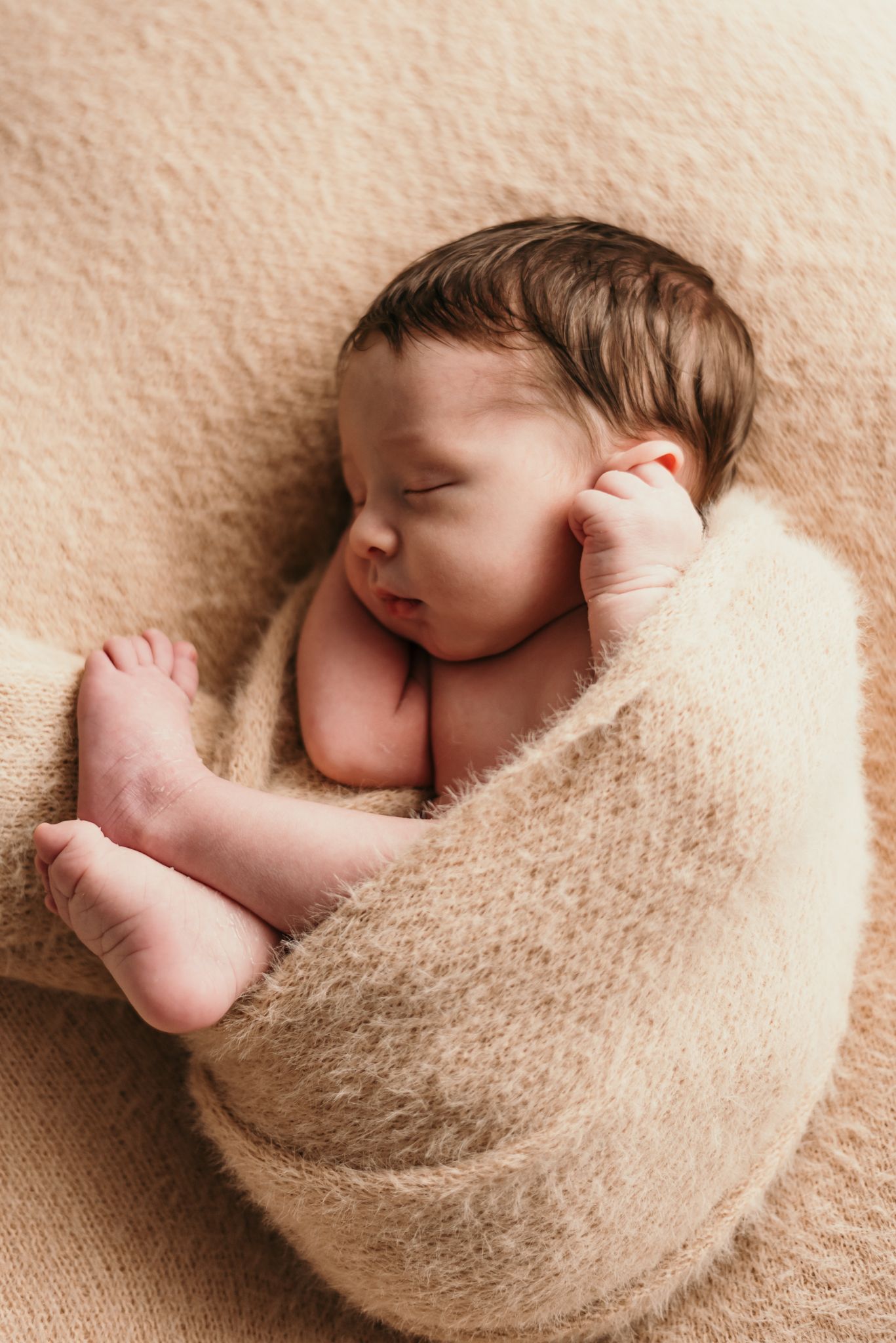 Sleeping newborn baby wrapped in beige blanket during peaceful nap.