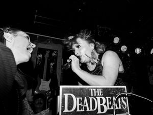 black and white image of a woman rockstar lead singer sings to a fan. Sign saying "The Deadbeats" in bottom middle of image