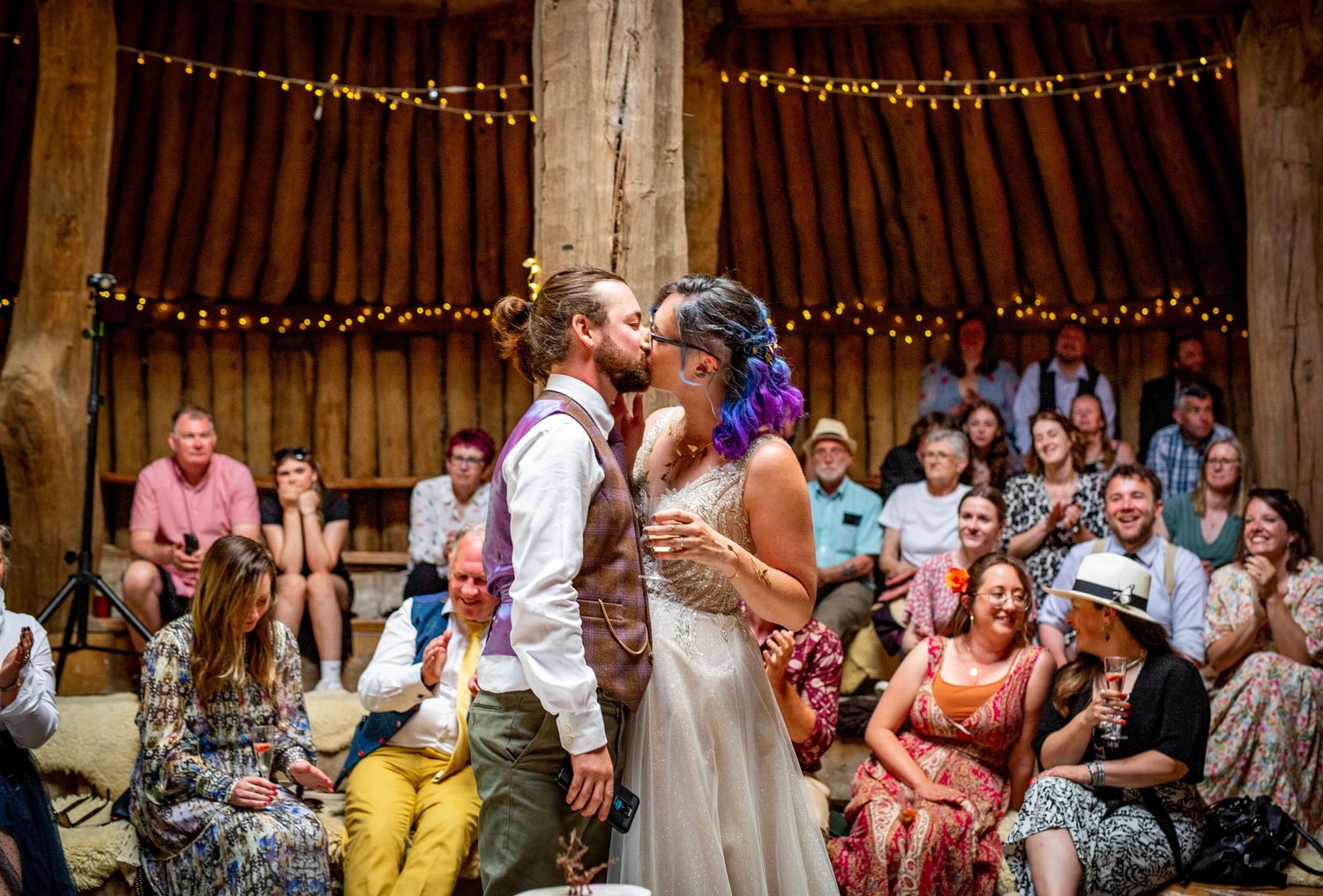 Wedding celebration inside a wooden barn with string lights and festive atmosphere.