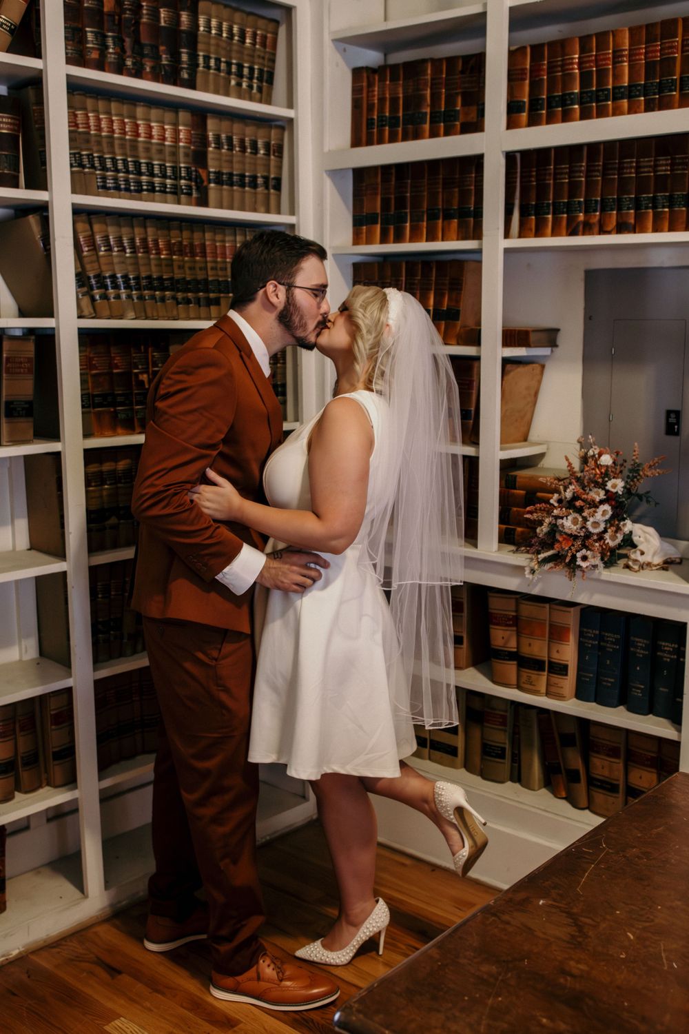 Newlyweds kissing in front of vintage law library bookshelves after courthouse elopement.
