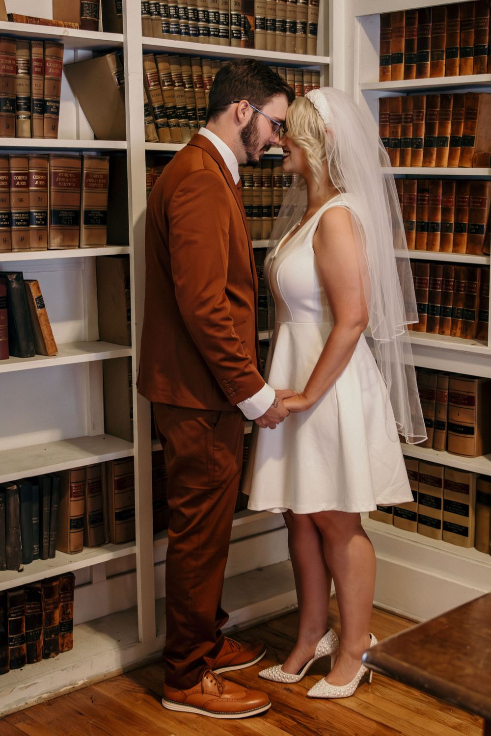 Bride and groom holding hands in front of law library bookshelves after courthouse wedding.