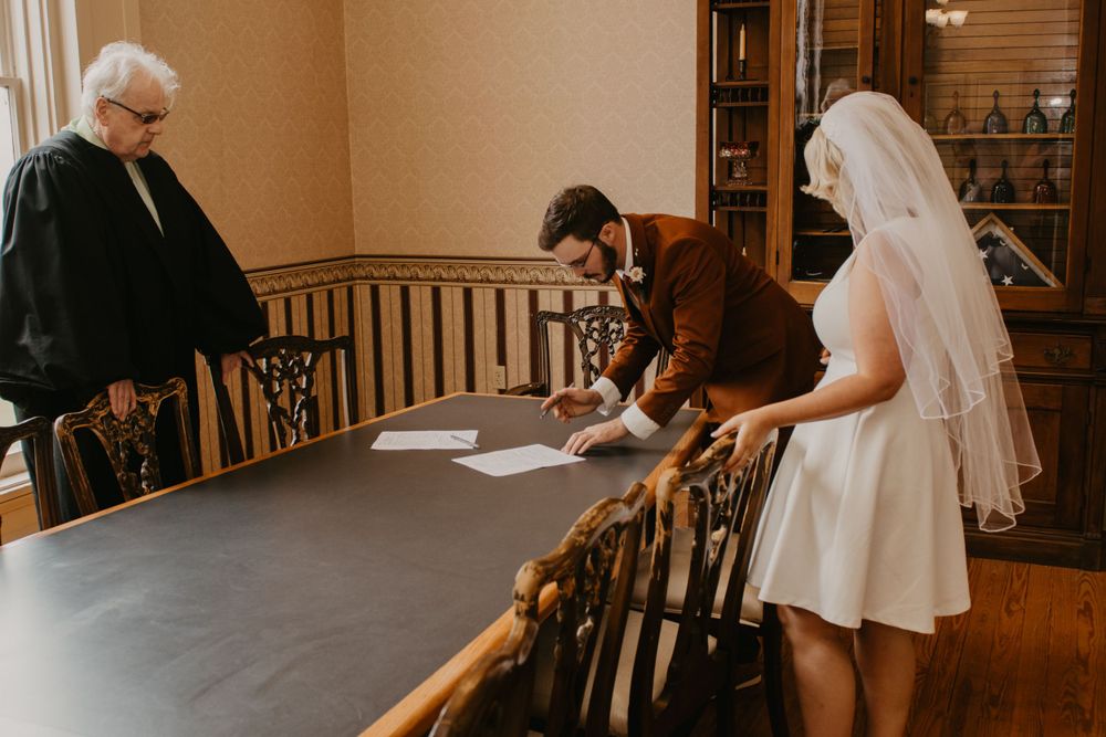 Bride and groom signing marriage license with officiant at courthouse wedding.