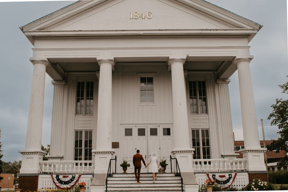 Bride and groom walk hand in hand toward a historic white columned wedding venue dated 1848.