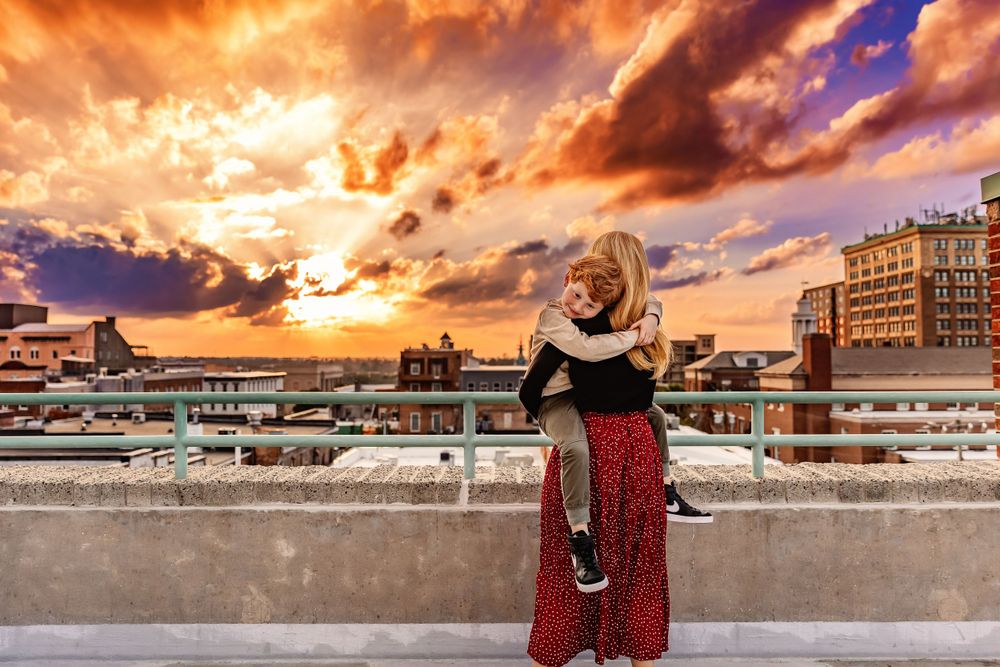 A couple poses against dramatic orange and purple sunset sky on an urban rooftop.