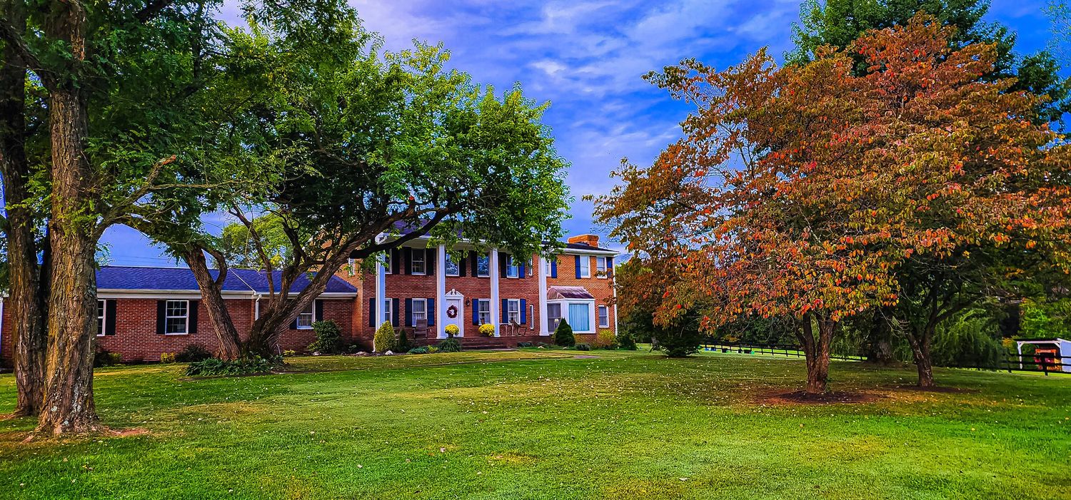 A grand red brick colonial house with fall foliage and manicured lawn.