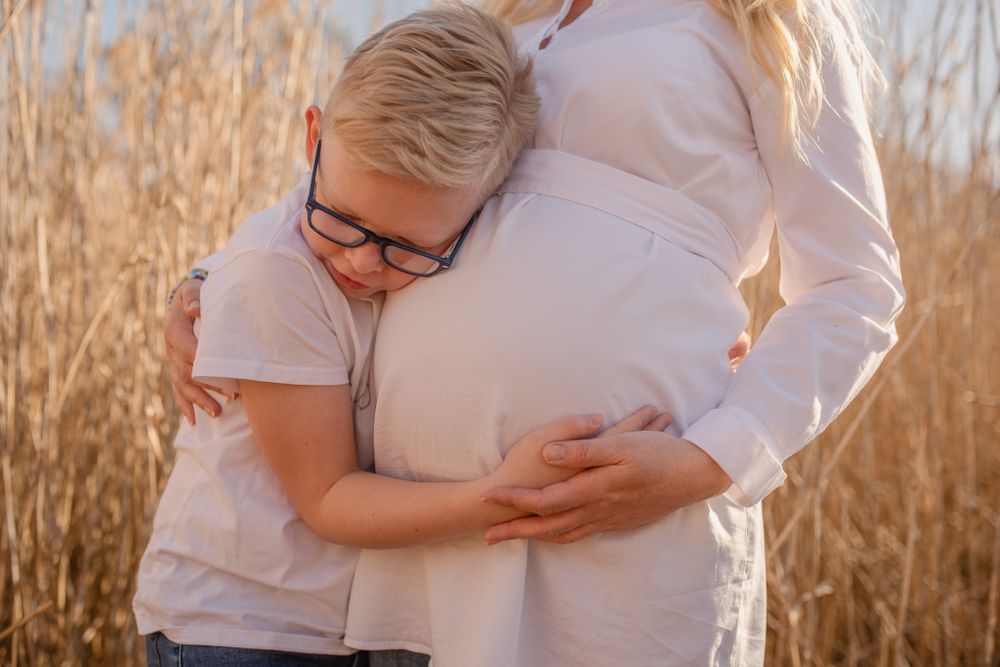 Intimate maternity moment captured in warm sunlight amongst dried reeds.