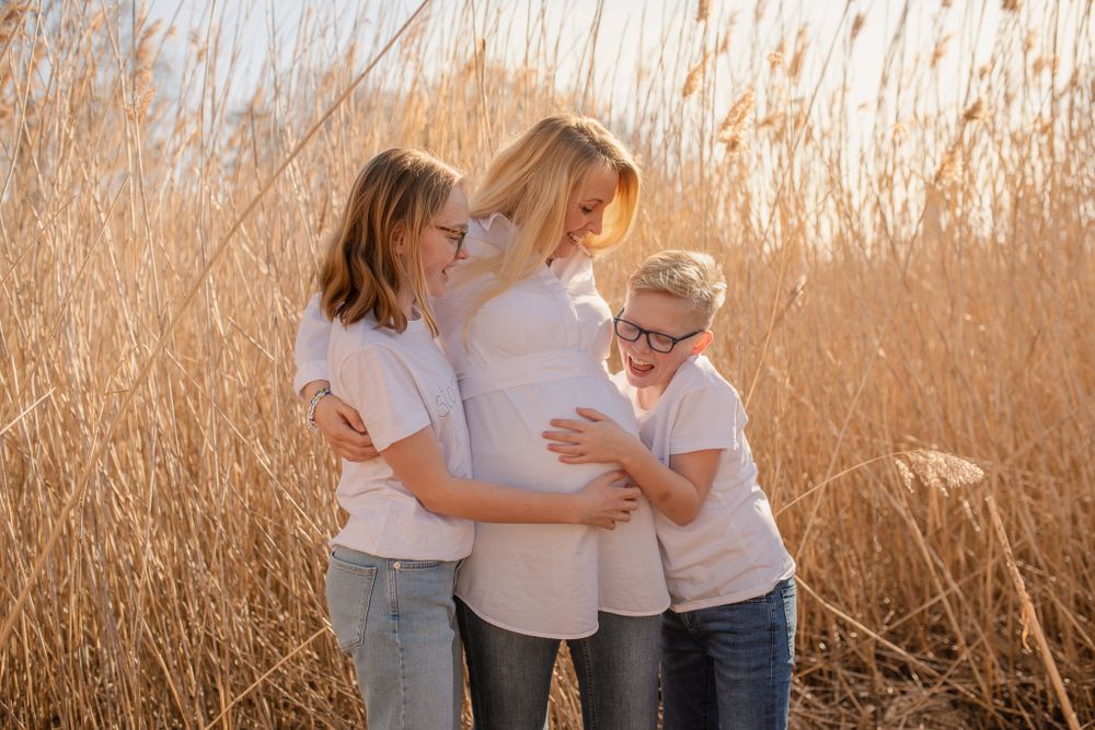 Family embracing during sunset maternity photoshoot in golden reed field.