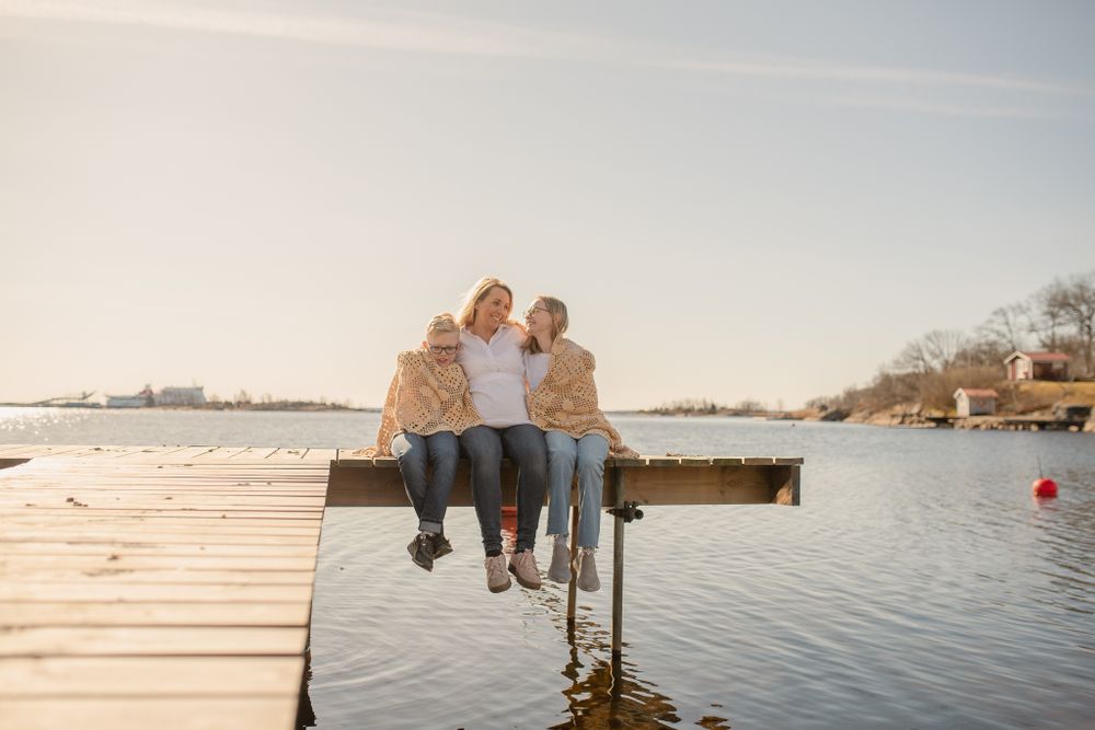 Two people sit close together at the edge of a wooden dock overlooking a serene lake at sunset.