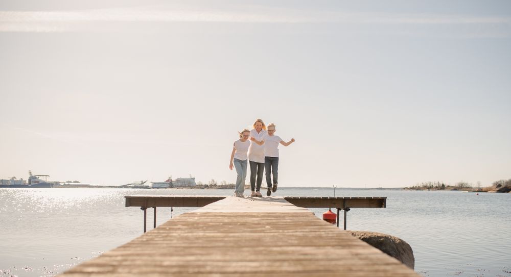 A couple stands together on a long wooden pier surrounded by calm waters and distant shoreline.