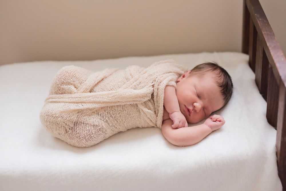 Sleeping newborn wrapped in cozy beige blanket on white bedding.