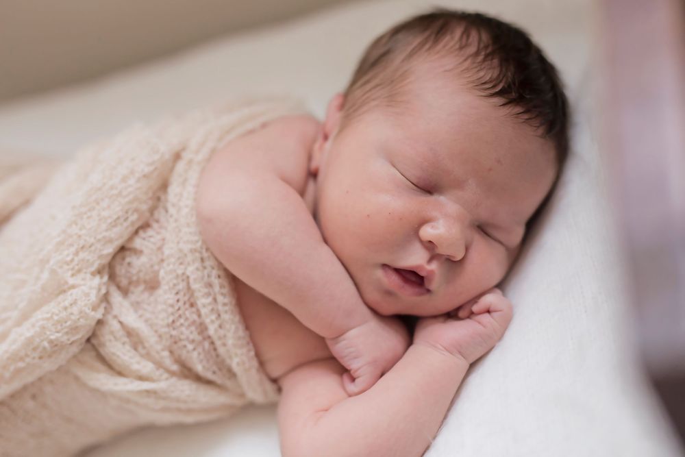 Peaceful newborn baby sleeping wrapped in soft beige blanket.