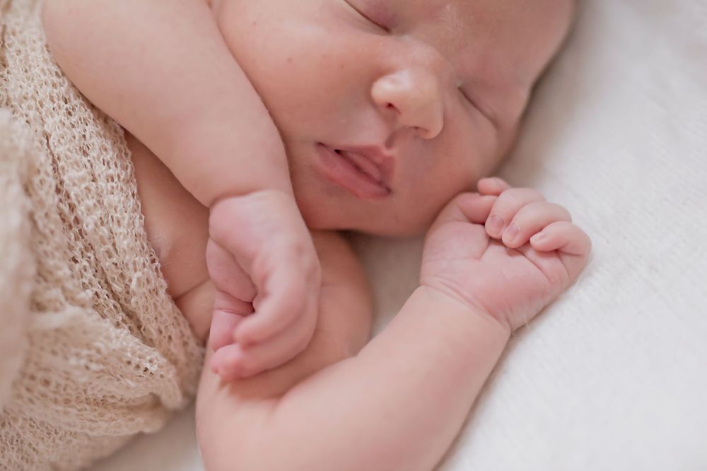 Close-up of newborn baby's tiny hands and feet wrapped in beige knit blanket.