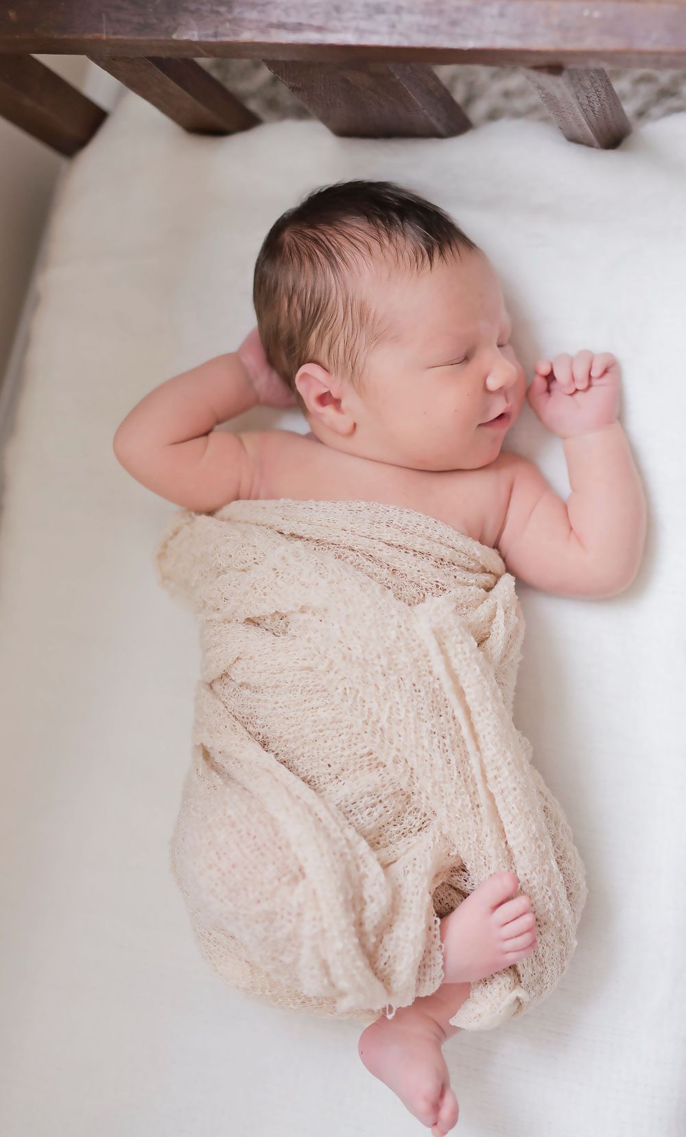 Sleeping newborn wrapped in soft beige knit blanket on white background.