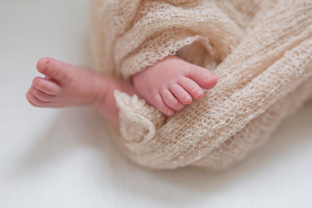 Tiny baby feet peeking out from cream colored swaddle wrap.