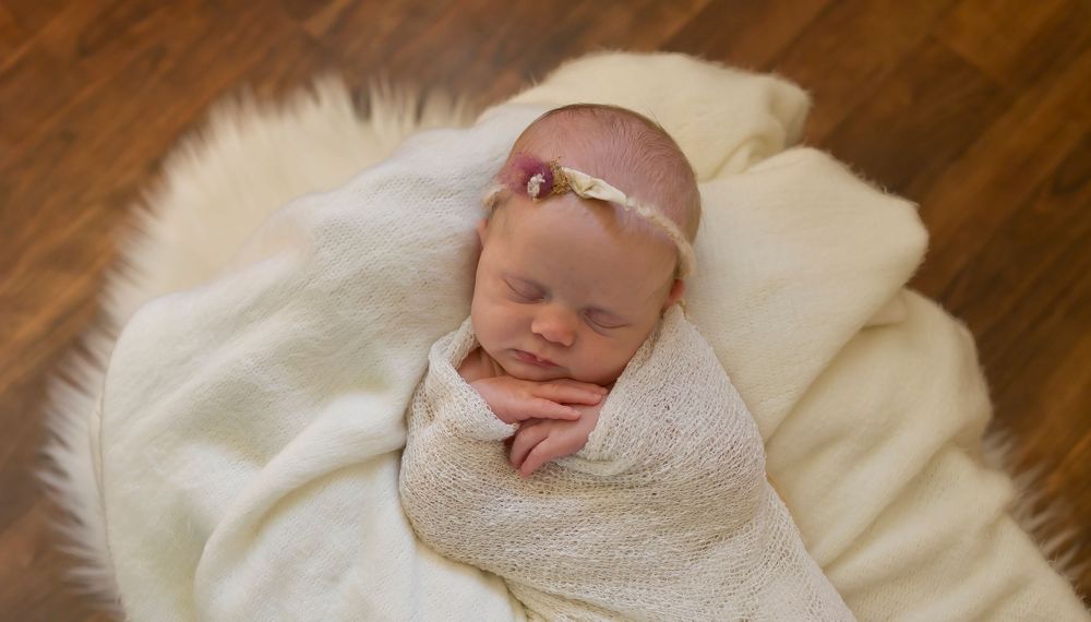 Newborn sleeping peacefully swaddled in white wrap on cream blanket.