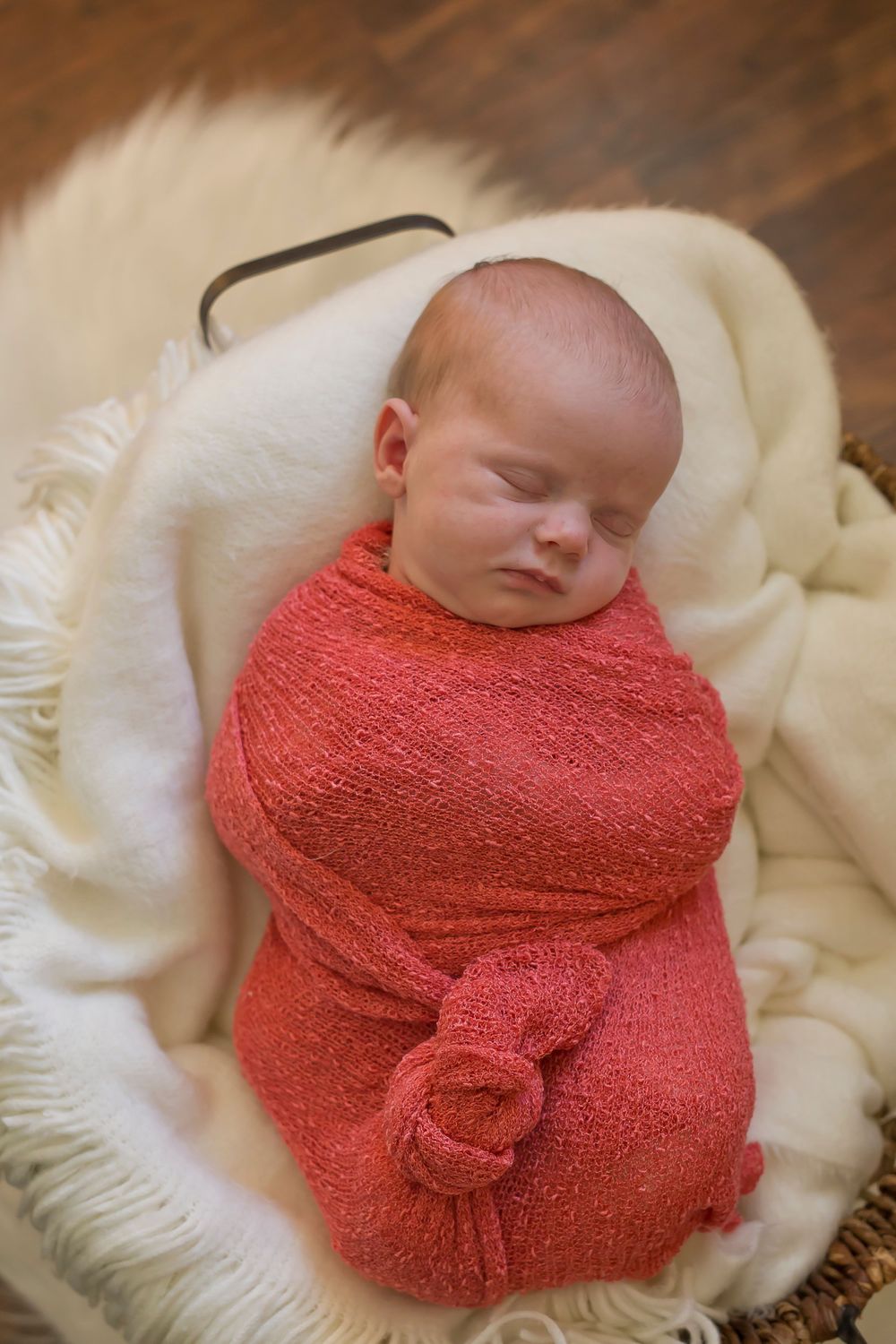 Peaceful newborn sleeping while wrapped in coral colored knit blanket.